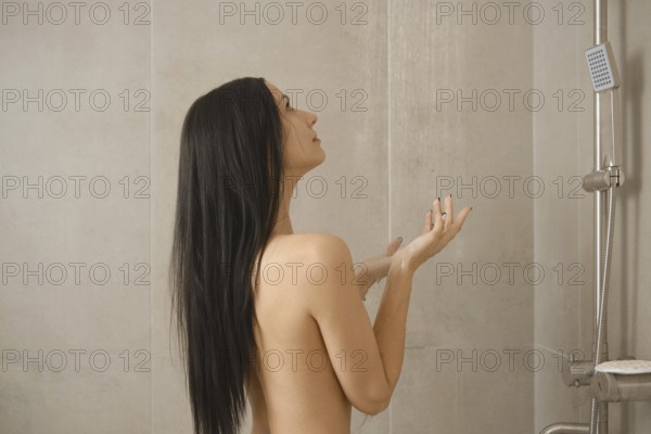 A woman stands underneath flowing water in a minimalist shower, enjoying a moment of peace. The