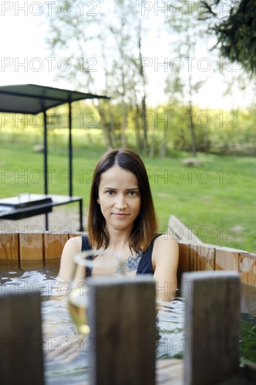 A woman enjoys a serene moment in a wooden hot tub, immersed in warm water, while surrounded by