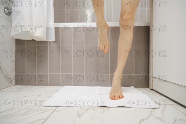 A person is stepping onto a white towel placed on the floor of a sleek bathroom after taking a