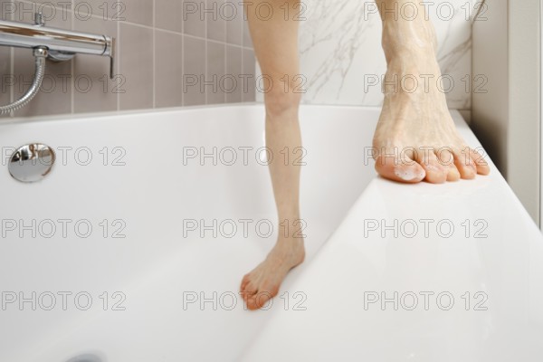 A person balances on the edge of a bathtub, showcasing a moment of daily life. The bathroom