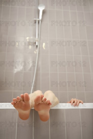 Feet sticking out over the edge of bathtub. The modern bathroom features light-colored tiles, and a