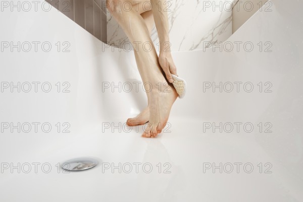 A person enjoys a moment of self-care, using a foot scrub in a clean, white bathtub. Natural light