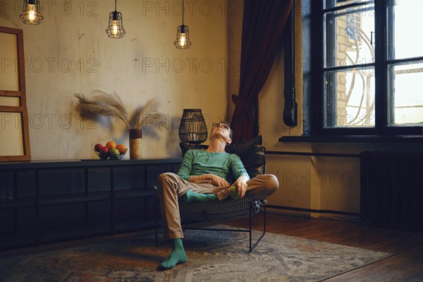 A man relaxes in a modern chair in a well-lit living space filled with warm tones. Sunlight streams