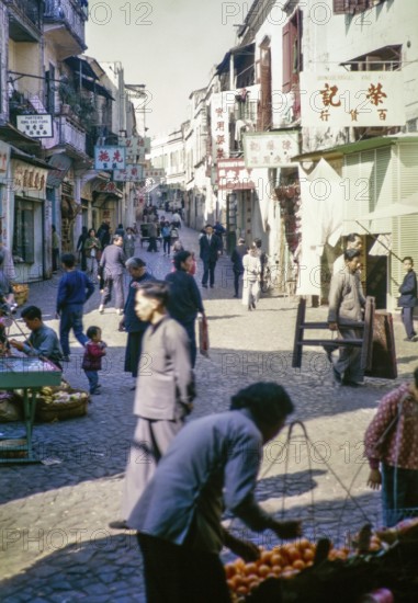Busy shopping street Cantonese shop signs, with people walking traders with fruit stalls, Macau,