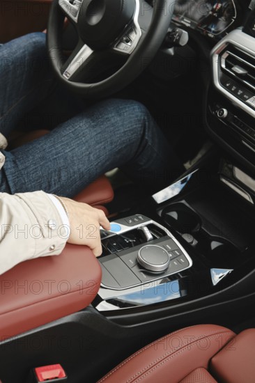 A person in casual attire sits in the driver's seat of a modern vehicle, reaching to adjust the