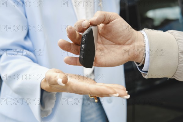 A person hands over car keys to another individual in a parking lot. The transaction takes place