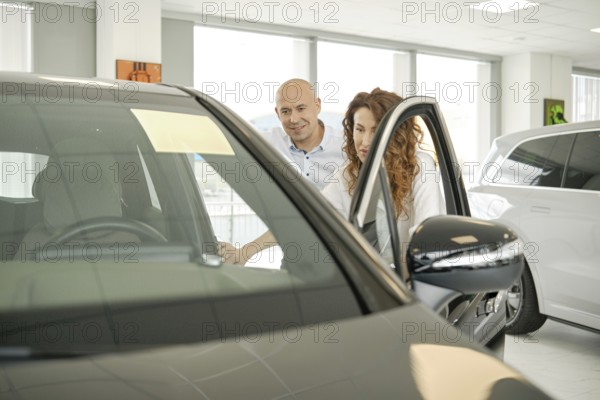 A couple is exploring options at a car dealership, looking closely at a vehicle. They appear