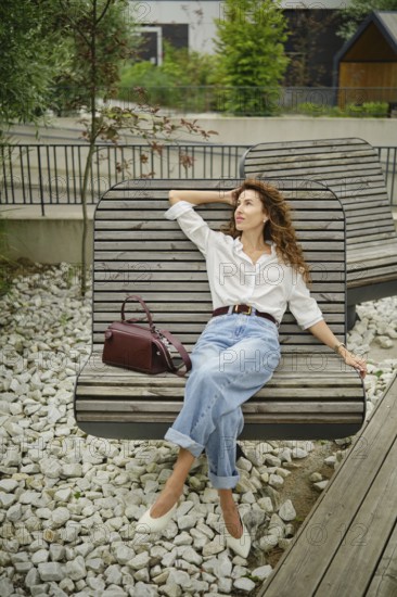 A woman enjoys her time on a stylish bench in a contemporary outdoor area filled with greenery. She