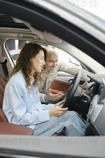 A woman sits in the driver's seat of a car, looking at the dashboard screen, while an older man