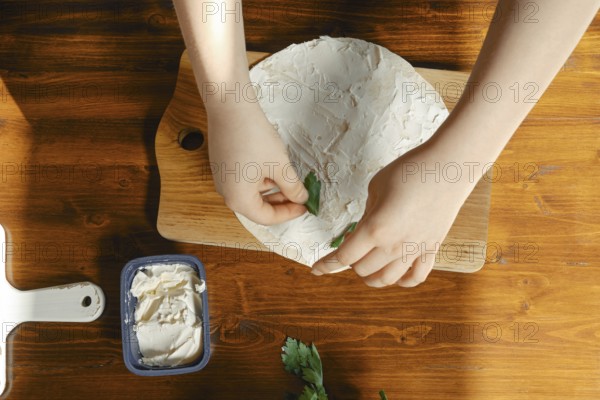 Hands carefully place fresh herbs onto a creamy spread during appetizer preparation. A container of