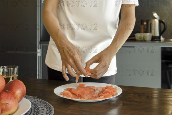 A person is arranging fresh salmon slices on a white plate in a stylish kitchen showcasing a focus