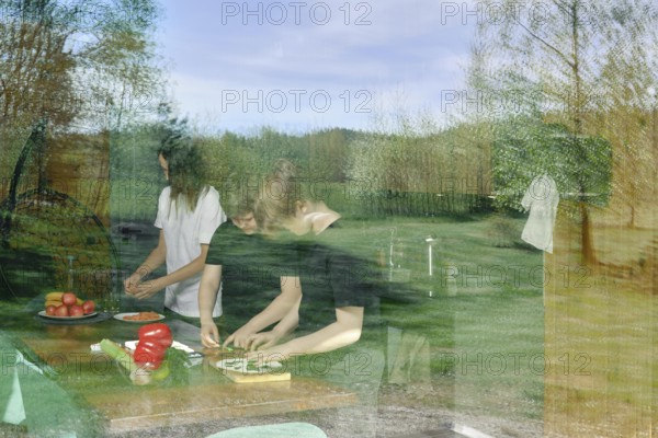 The view through the window to the kitchen, where the family is preparing a light snack. The glass