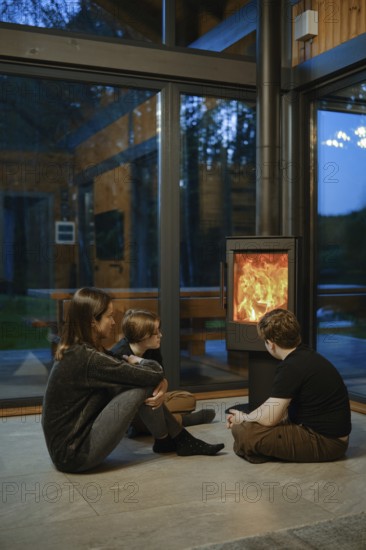 A family of three gathers around a glowing fireplace inside a contemporary cabin. The warm ambiance