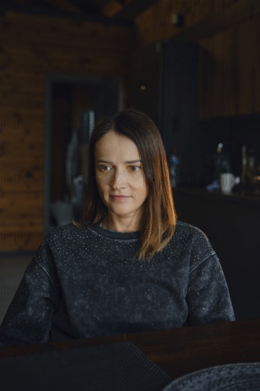 A woman with medium-length brown hair sits at a dark wooden table, reflecting thoughtfully. The