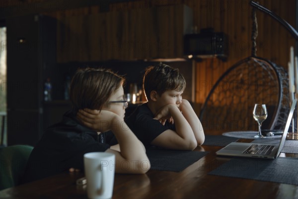 Two children are seated at a wooden table in a warm, rustic environment, deeply engaged with a