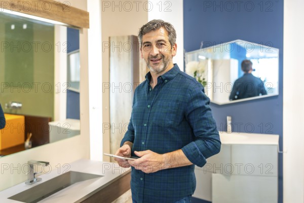 Smiling mature male architect using a digital tablet while choosing bathroom fixtures in a home