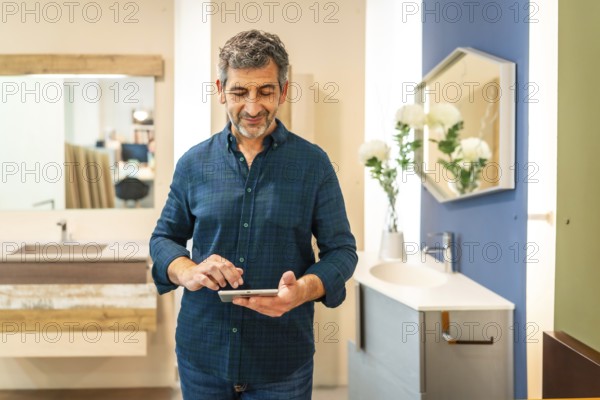 Mature architect using digital tablet choosing bathroom fixtures in home improvement store, smiling