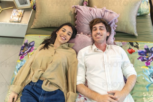 Young couple smiling and lying on a bed, testing comfort together while shopping for home goods in
