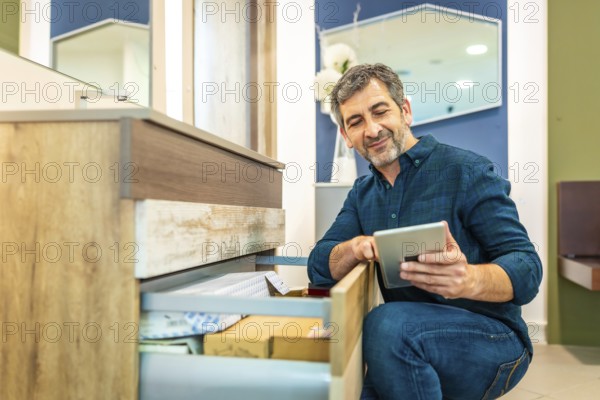 Smiling mature man using a digital tablet while checking out furniture options in a bathroom