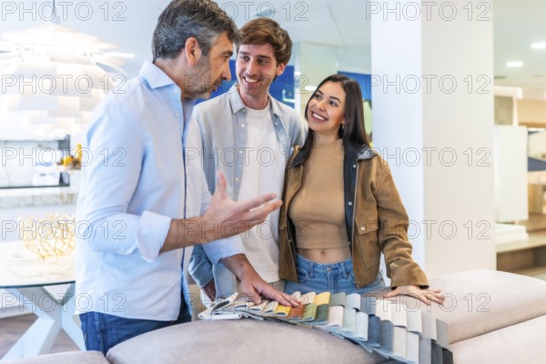 Couple and salesman discussing upholstery fabric swatches in furniture store, exploring options for