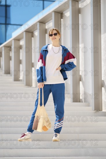 A young woman stands on a series of outdoor steps, wearing a colorful sports outfit with sunglasses