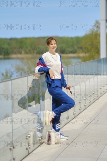 A woman dressed in comfortable sportswear leans casually against a glass railing overlooking a