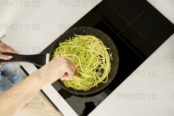 Cooking spiralized zucchini on a stovetop in a modern kitchen during daylight hours