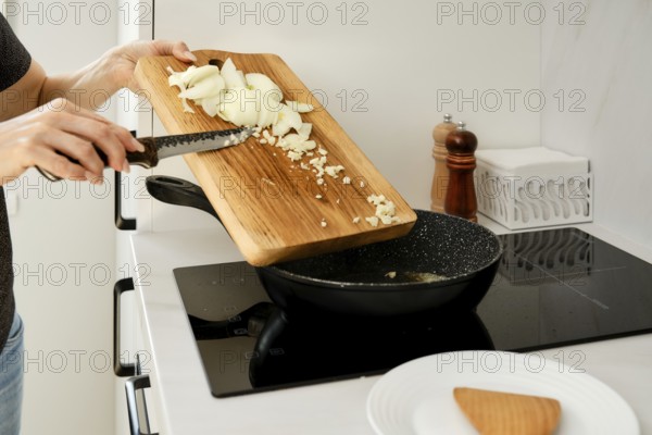 An unrecognizable woman laid out chopped onions and garlic in a frying pan. She is preparing the