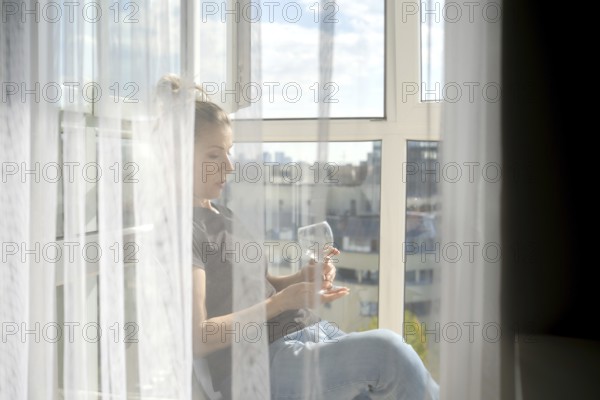 Sunlight streams through sheer curtains as a woman sits peacefully by the window. She gazes