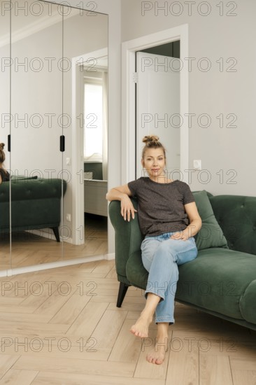 A woman sits comfortably on a green couch in a modern living room. She poses casually, with her