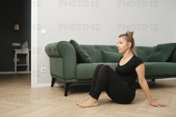 A woman dressed in comfortable workout attire is seated on the floor in a living room. She engages