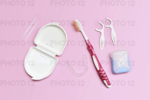 Top view of dental clear aligners, toothbrush, toothpicks and floss on pink background with copy