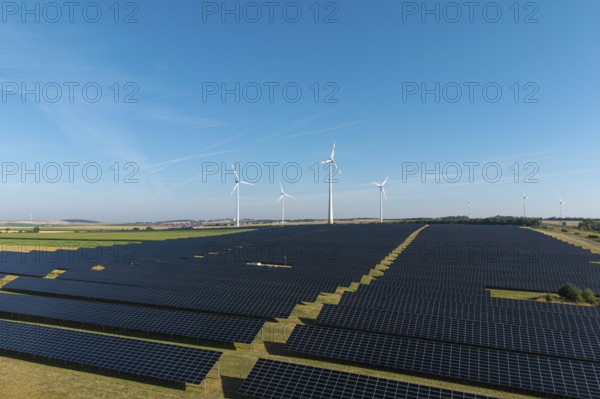 Field full of solar panels with wind turbines in the background under a clear sky, near Kitzingen,