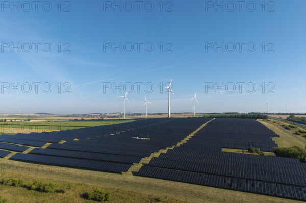 Large-scale solar panels and wind turbines across a wide agricultural field, near Kitzingen, Lower