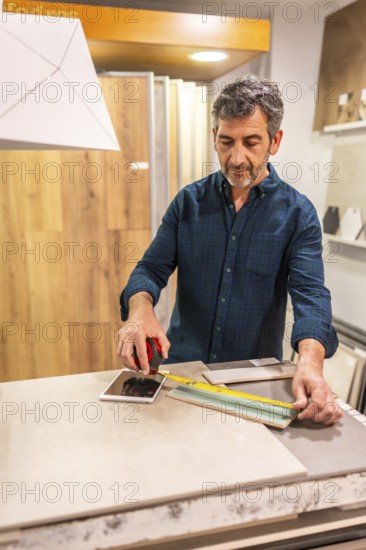 Architect taking measurements of ceramic tile using a tape measure and tablet in a home improvement