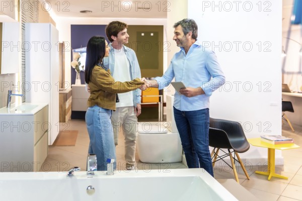 Couple shaking hands with salesman using digital tablet in bathroom furniture store, finalizing
