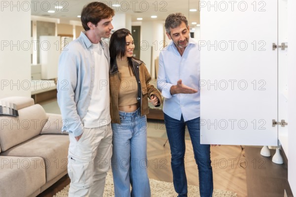 Smiling shop assistant showing a white cabinet door to a young couple, helping them choose