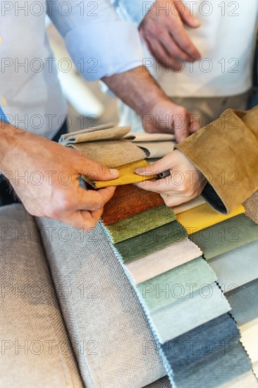 Customers and sales assistant choosing upholstery fabric from a wide variety of colors and textures