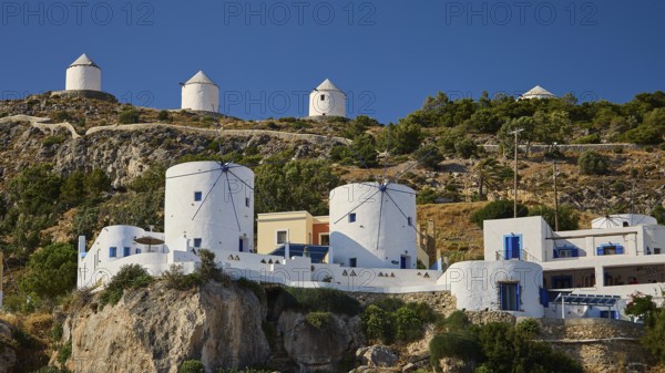 Traditional white windmills on a hill surrounded by Mediterranean architecture and vegetation,