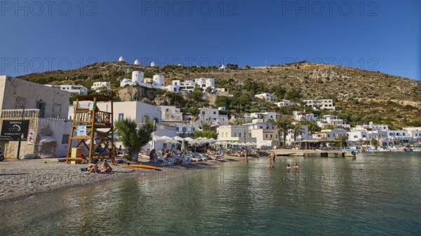 Beach promenade on a clear blue sea, behind it Mediterranean town and windmills on hill, Pandeli