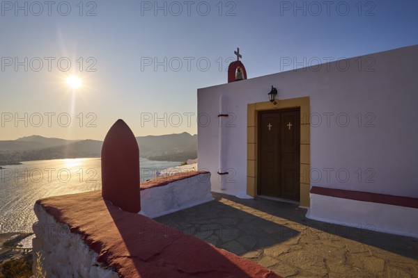 Chapel with cross by the sea at sunset, peaceful atmosphere and classic Greek architecture, red