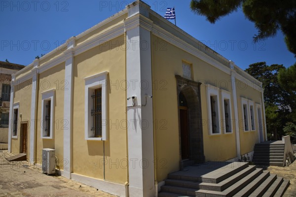 Yellow building with flag, surrounded by trees. Historic architecture with white window frames,
