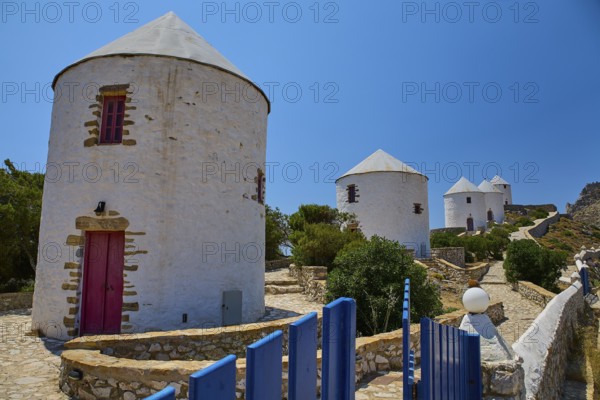 White windmills with red doors and fence under a blue sky on a sunny island, Pandeli Castle,