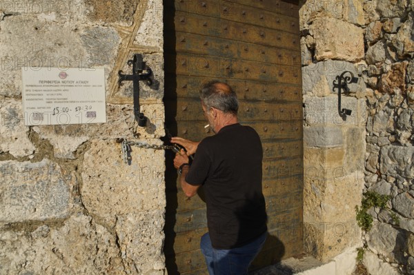 Man opens antique, massive wooden gate in stone wall, Pandeli Castle, Castle, Leros Fortress, St