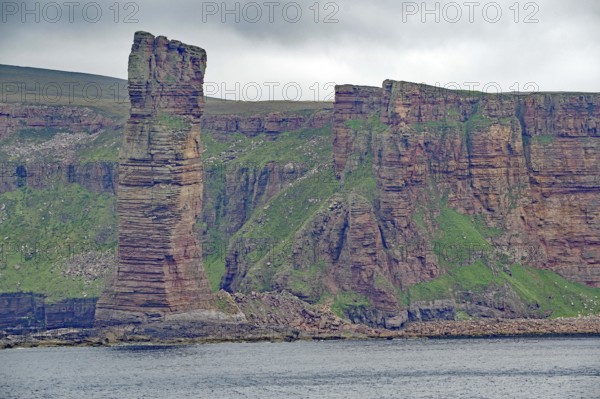 Impressive rock formations on the coast in contrast to overgrown green hill under cloudy sky, Old