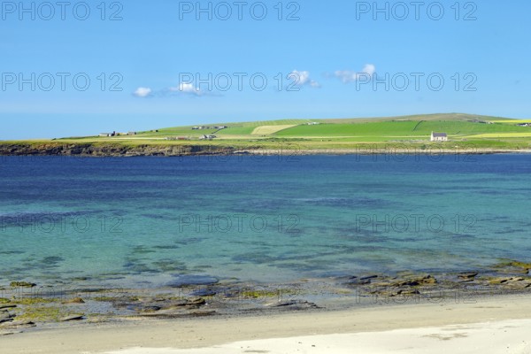 Clear blue sky over a coastal landscape with green shore and crystal clear water, Skara Brae,
