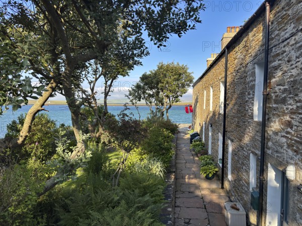 Small stone cottage with garden and sea view in sunny weather, surrounded by nature, Stromness,
