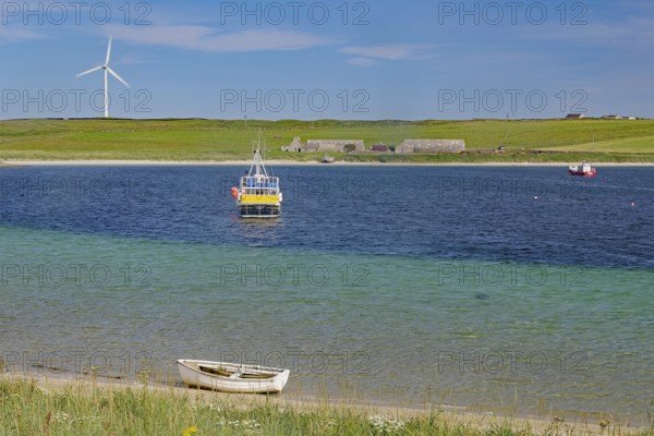 Colourful coastal landscape with boat, windmill and vast water under blue sky, Lambholm, Orkney