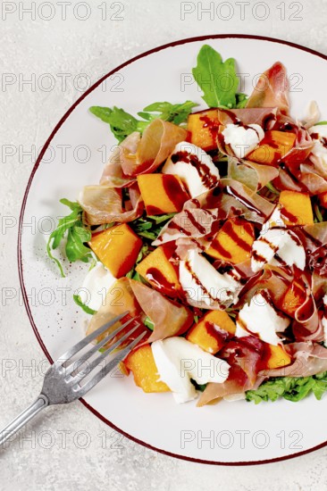 Salad with slices of ripe melon, prosciutto, mozzarella and fresh arugula, decorated with balsamic
