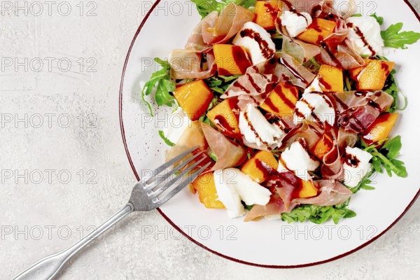 Salad with slices of ripe melon, prosciutto, mozzarella and fresh arugula, decorated with balsamic